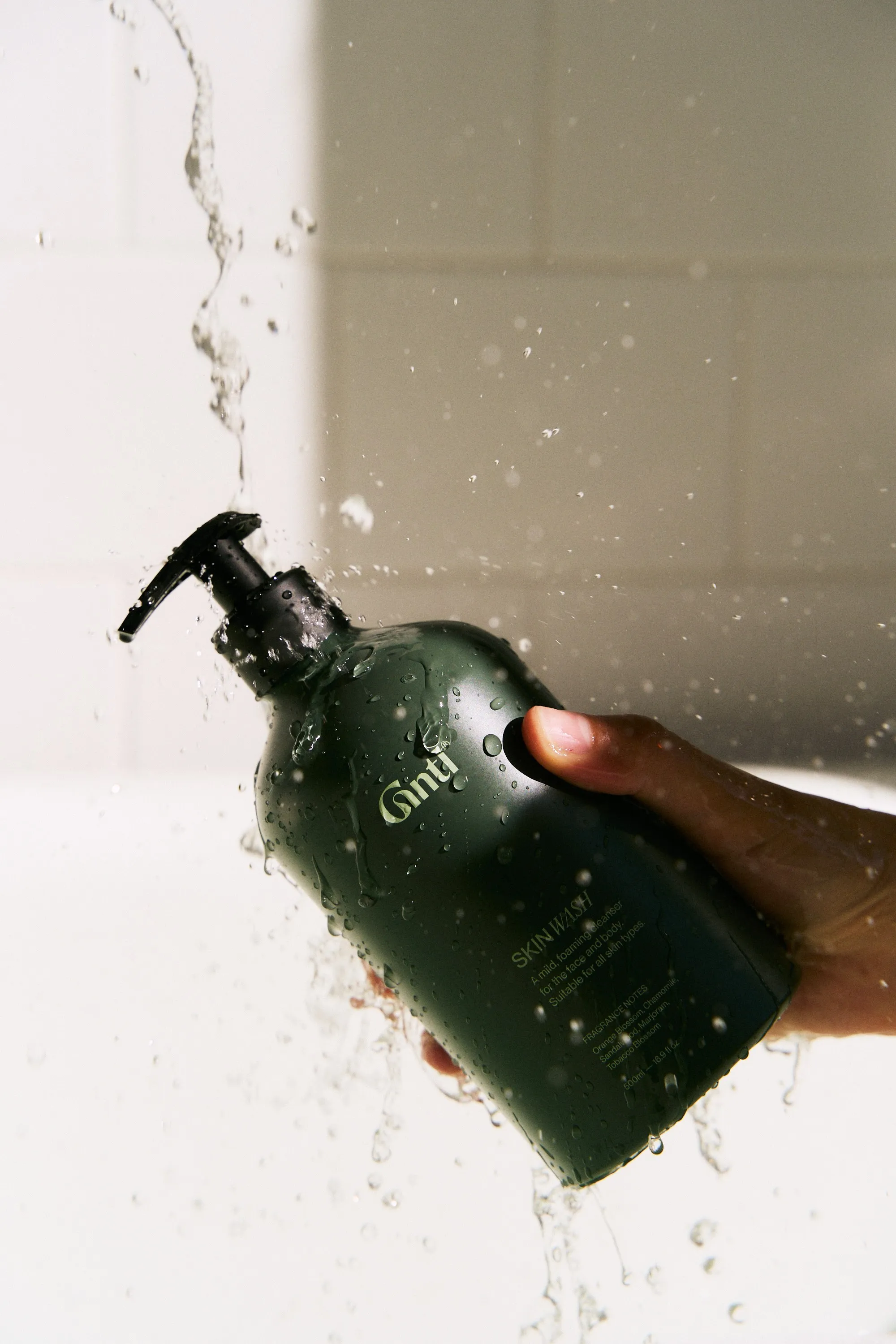 Hand holding a dripping Gntl bottle under a stream of water