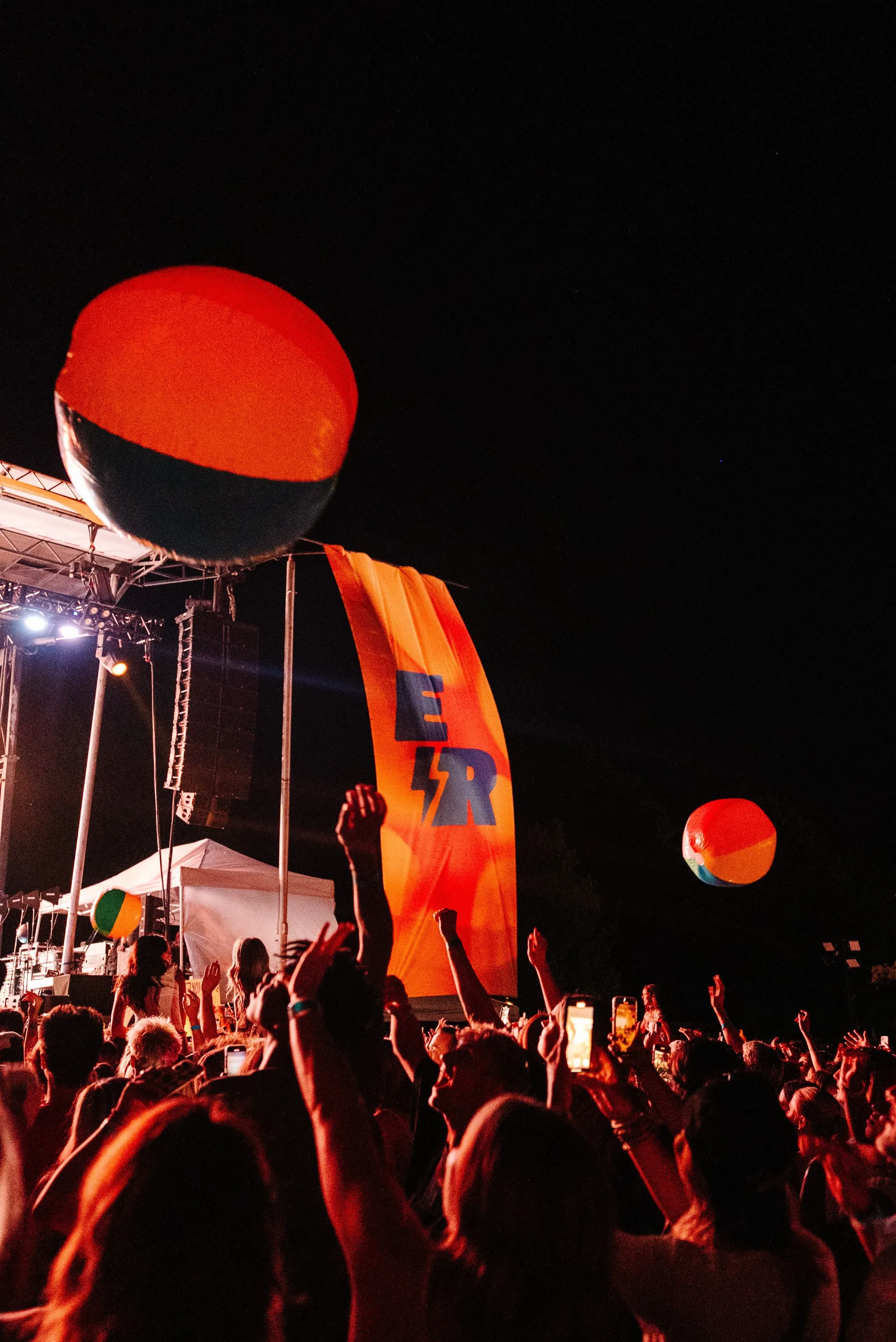 Night crowd with beach balls beside an orange ER banner at Electric Revival