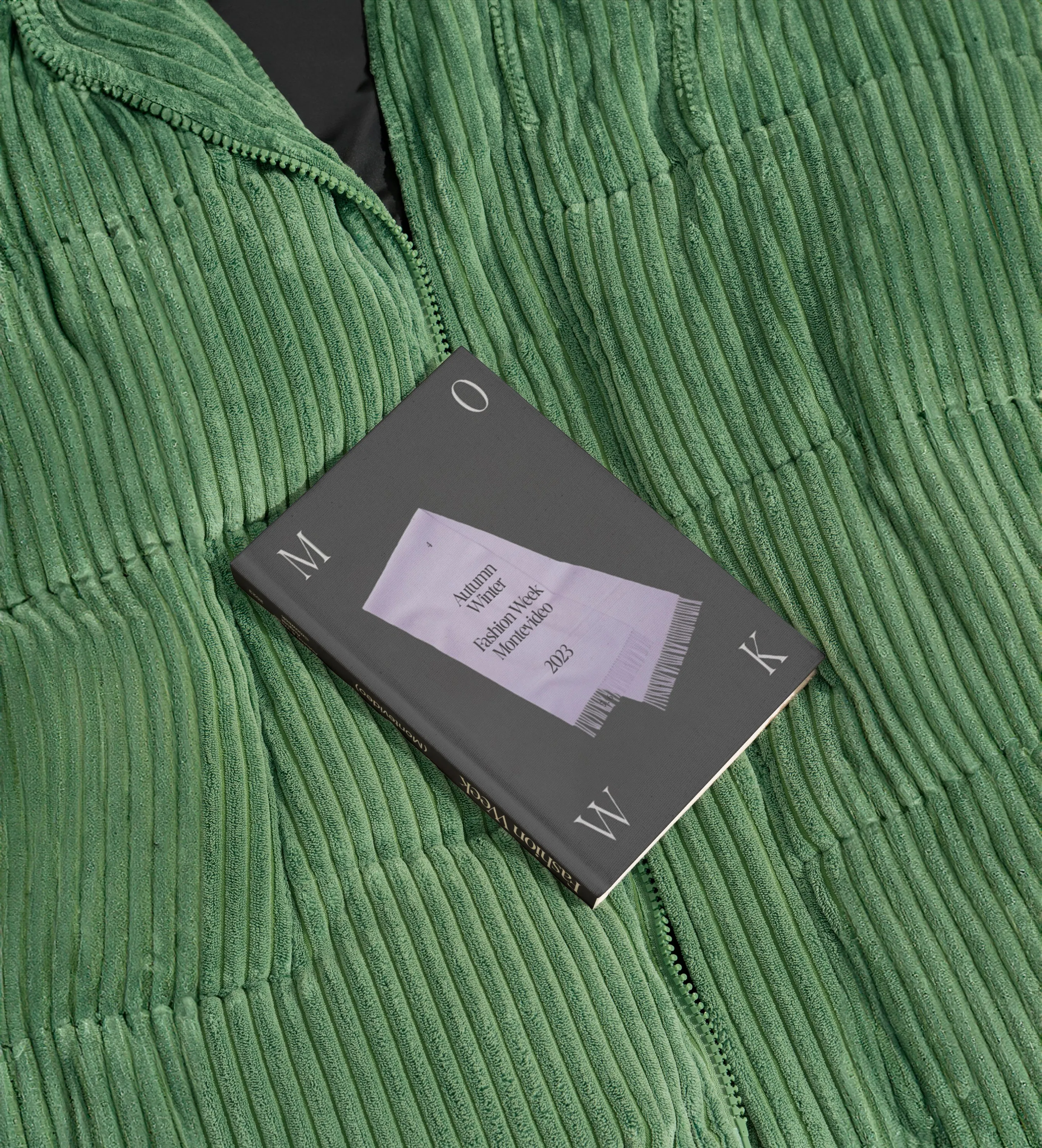 Moweek '23 grey lookbook resting on a green corduroy jacket
