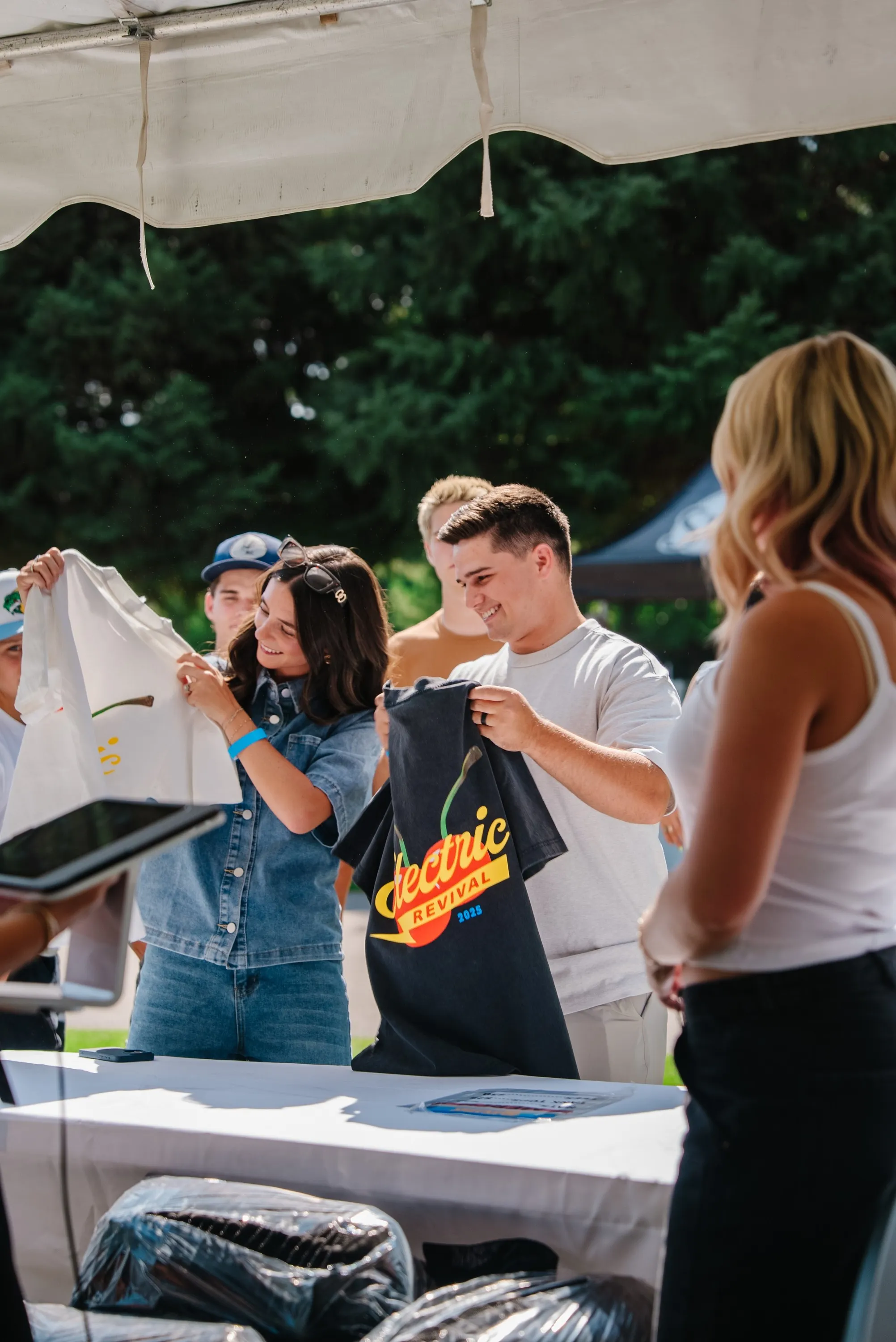 Fans holding up Electric Revival merch tees at a tented table