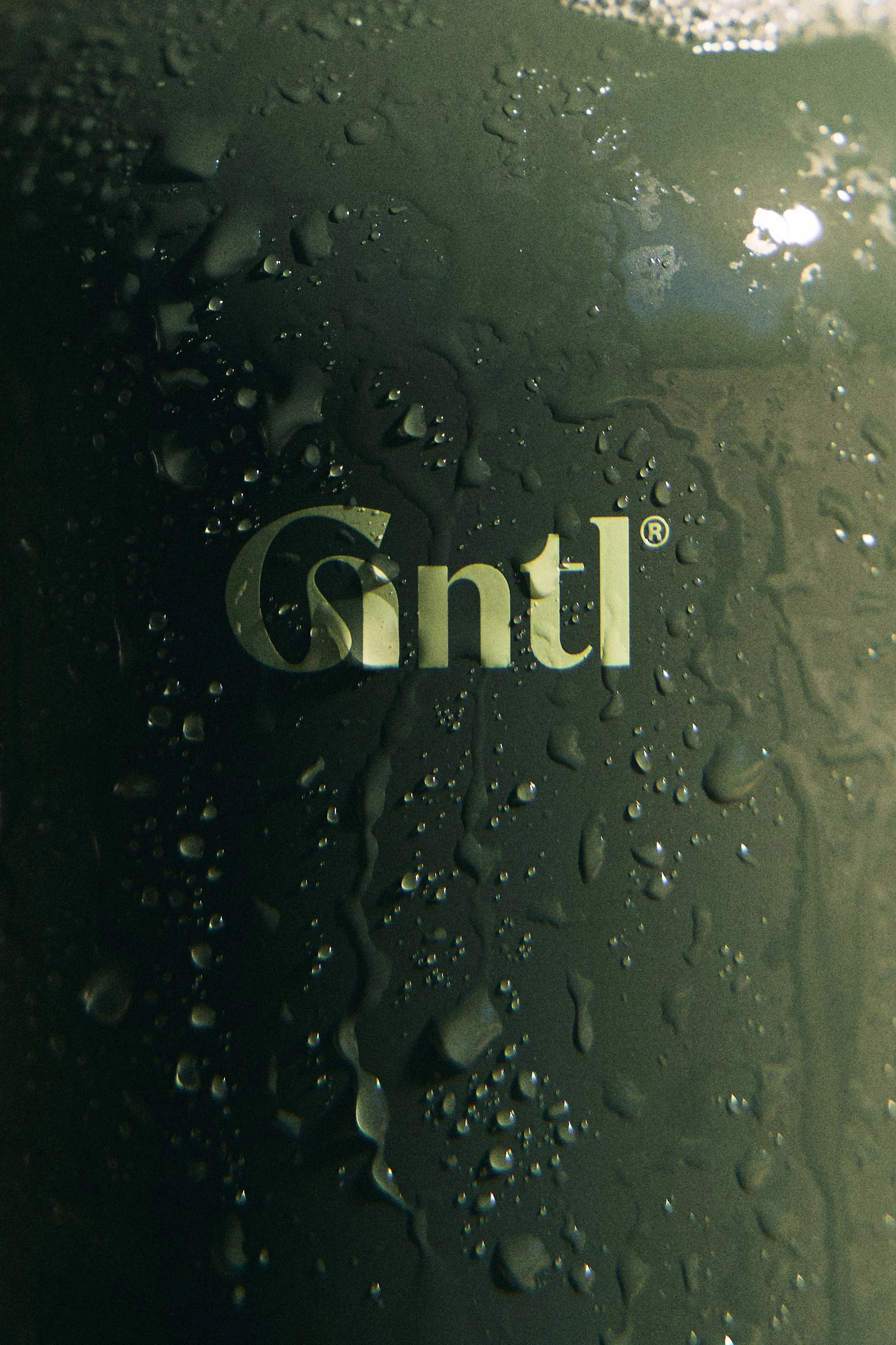 Gntl logo in pale green on a wet dark green bottle surface
