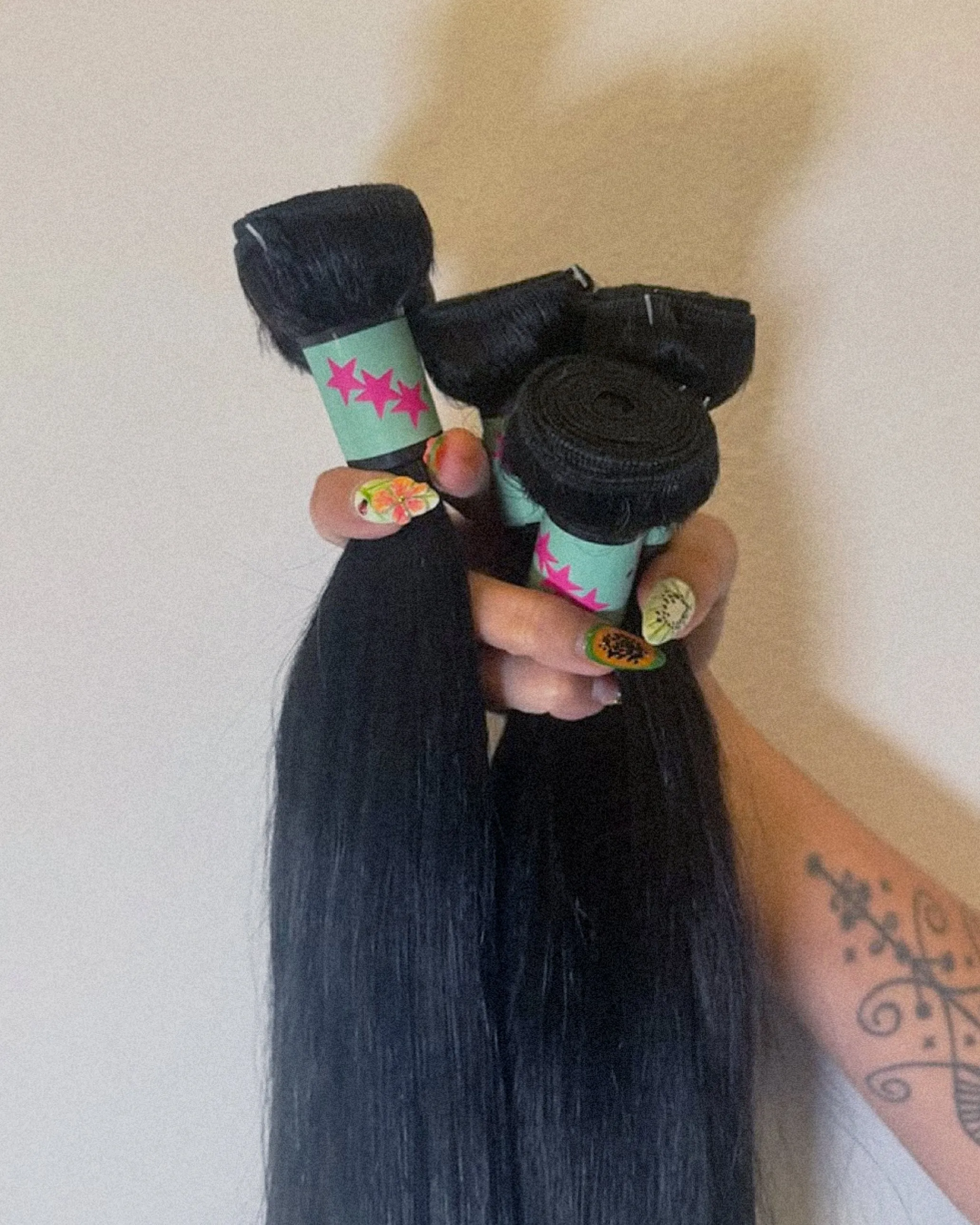 Hand holding black hair bundles wrapped in aqua bands with pink stars