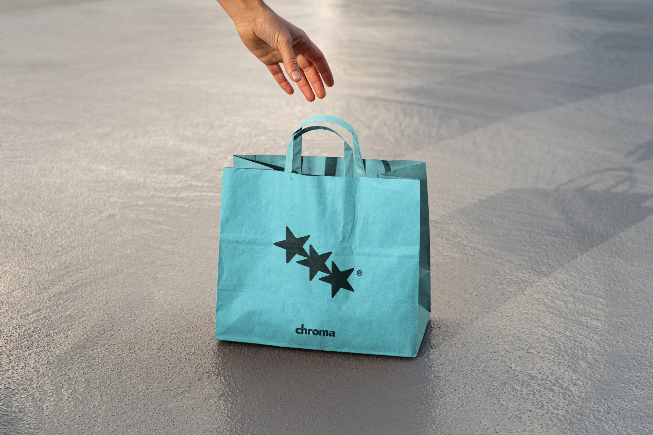 Aqua Chroma shopping bag with three stars, a hand reaching down for it