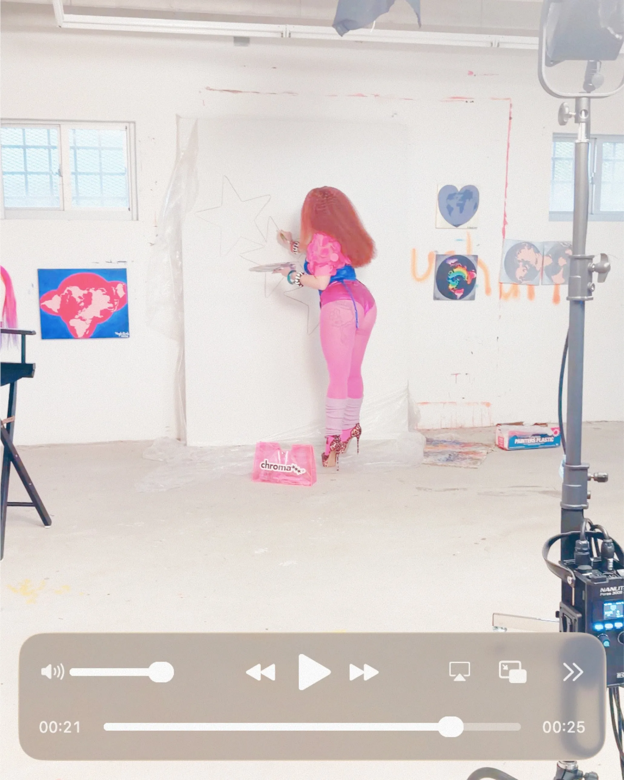 Campaign film still: a woman in pink painting stars on a studio wall beside a pink Chroma bag