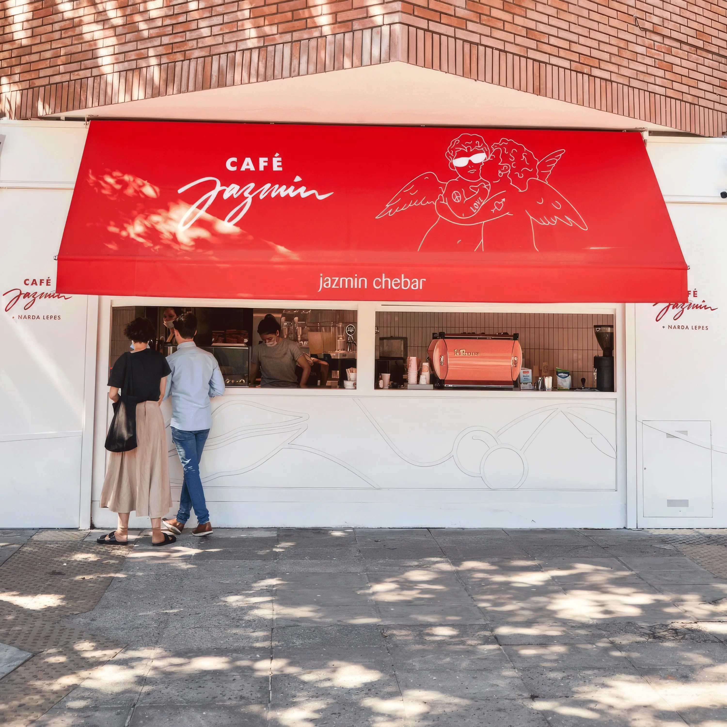 Café Jazmín storefront with red awning and angel illustration, customers at the window
