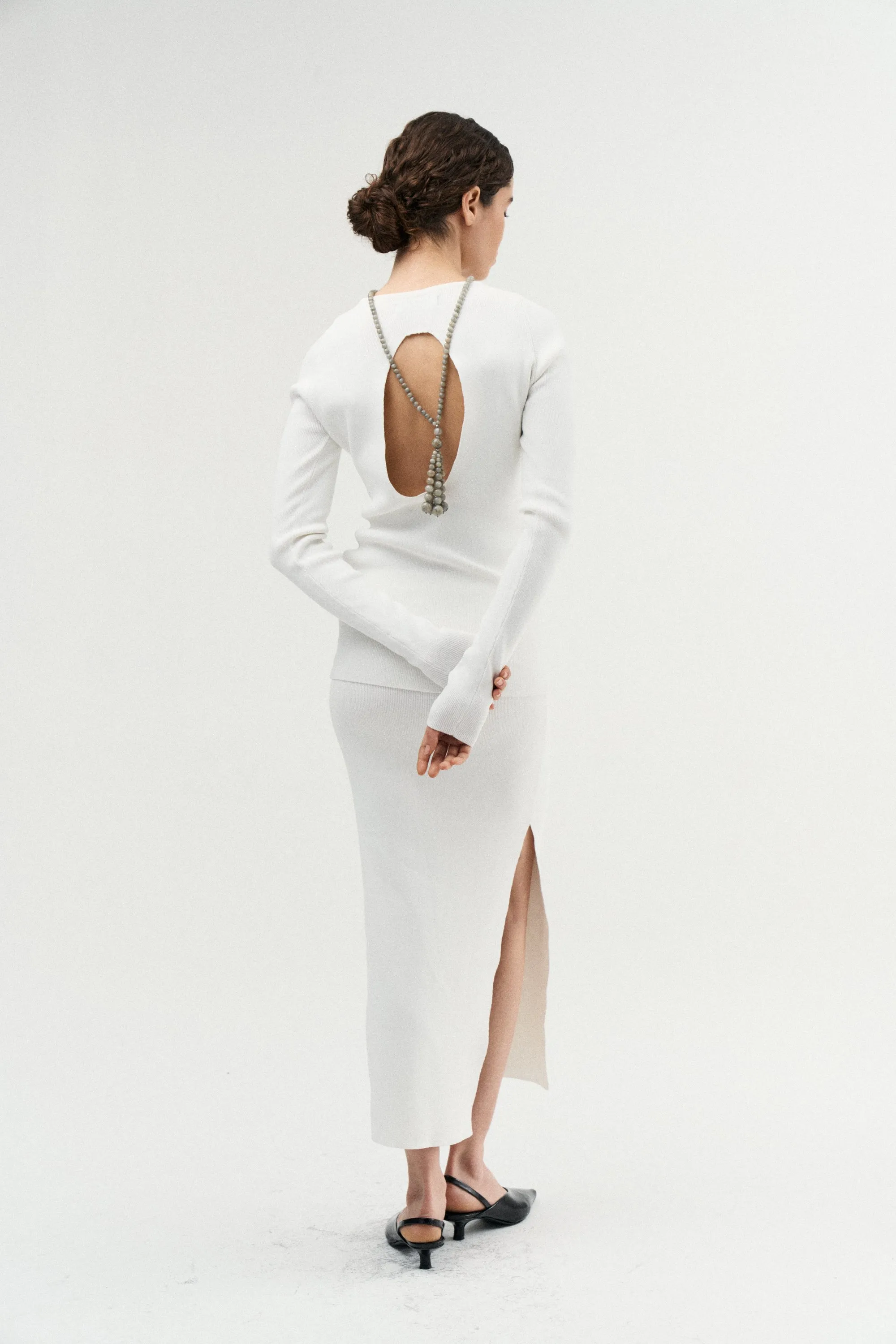 Model from behind in a white open-back dress with a chain falling down her back