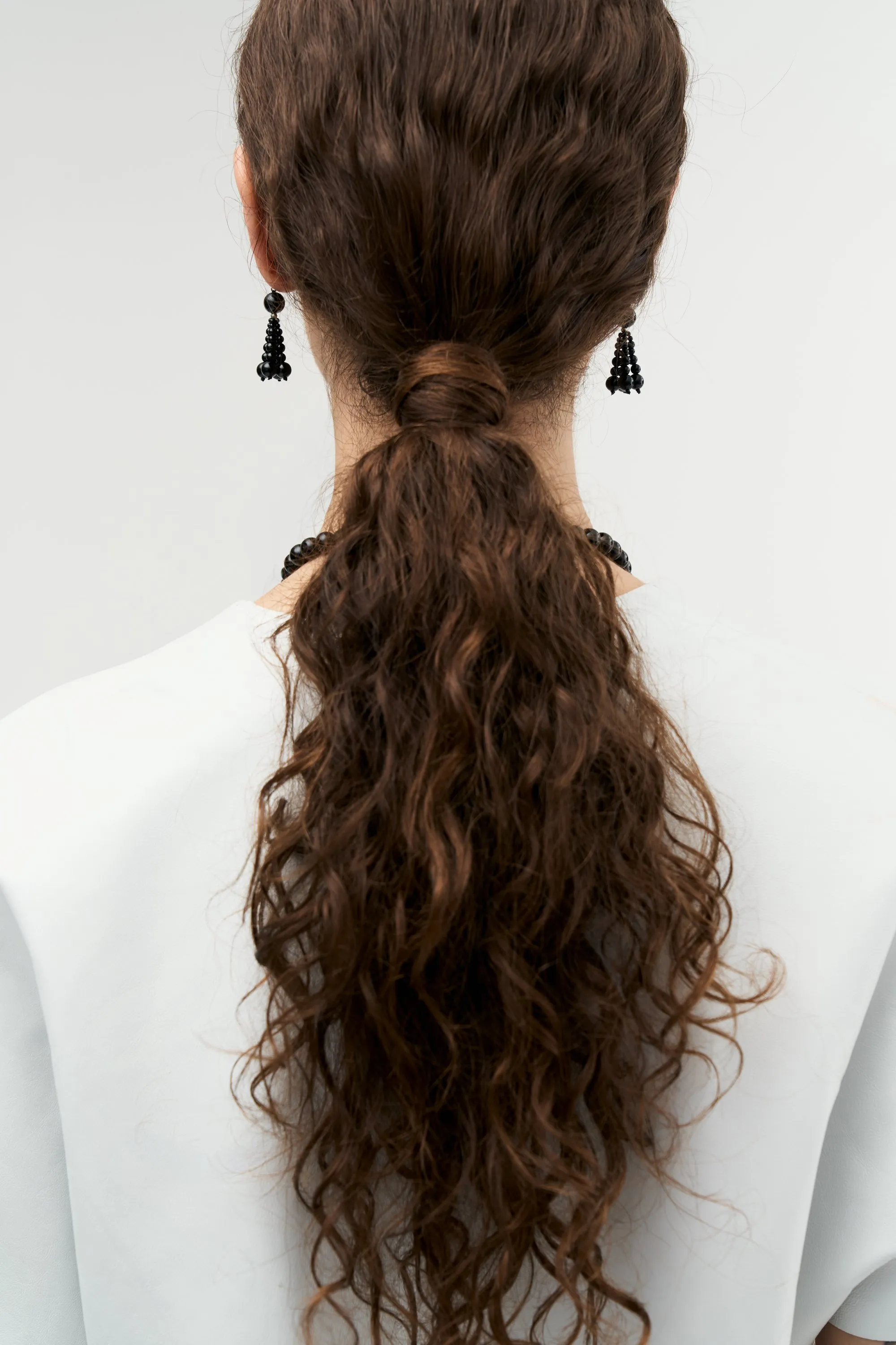 Model from behind with a long curly ponytail and black beaded drop earrings