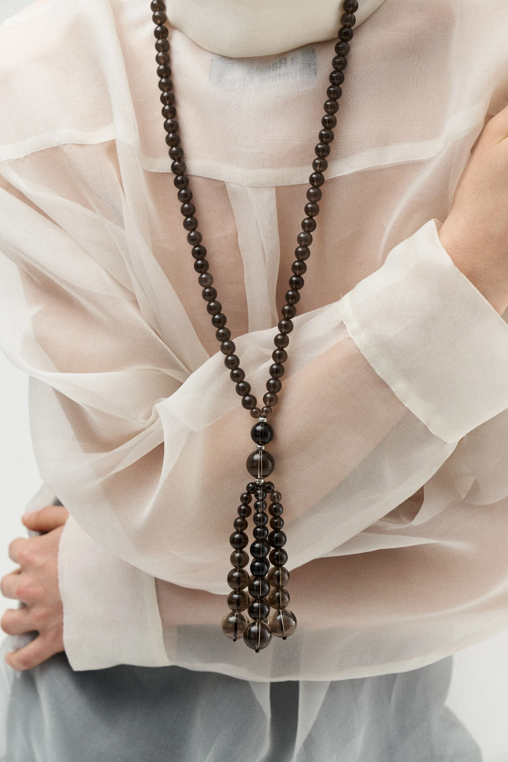 Long smoky quartz bead necklace with tassel over a sheer white shirt