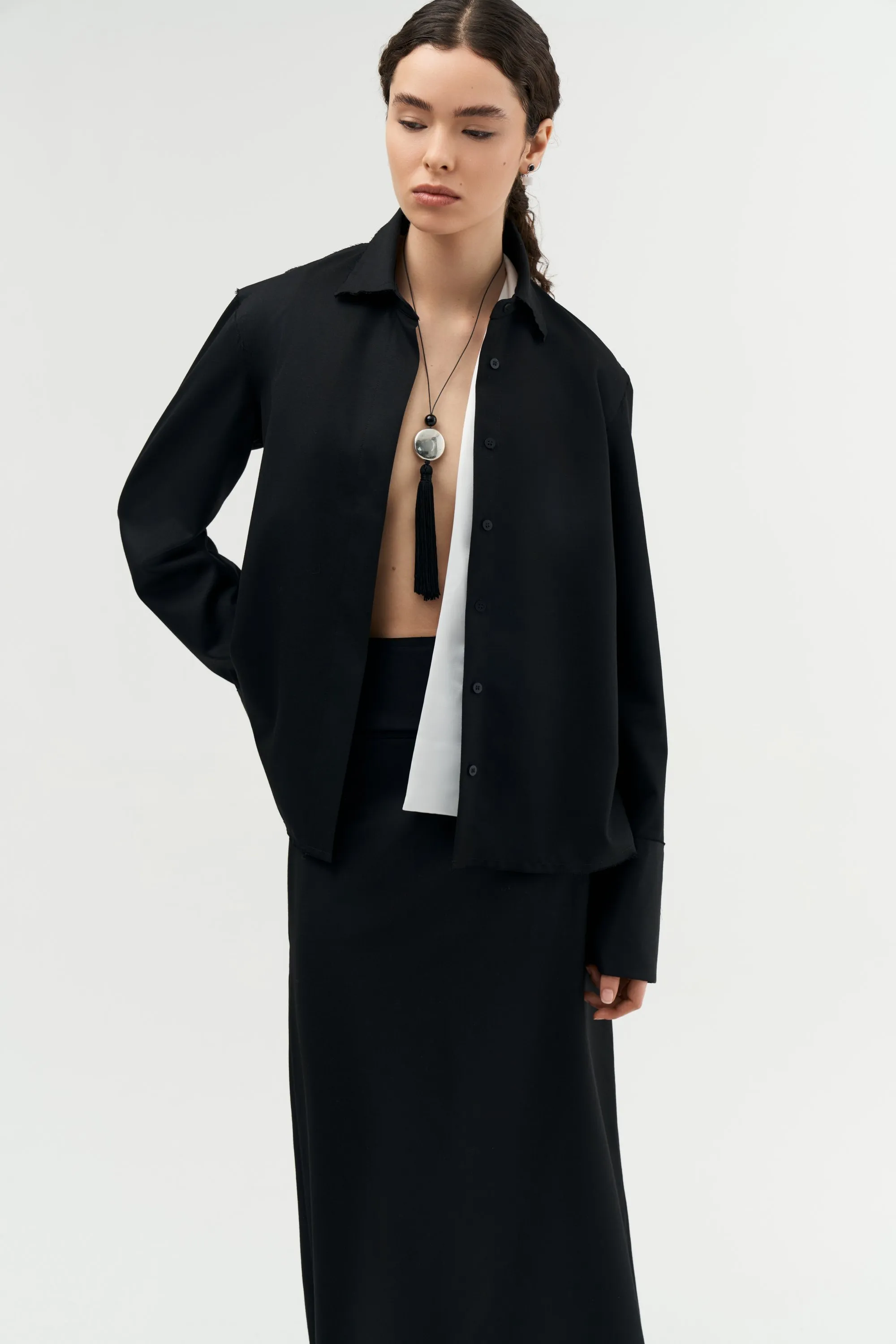 Model in a black jacket and skirt wearing a pendant necklace