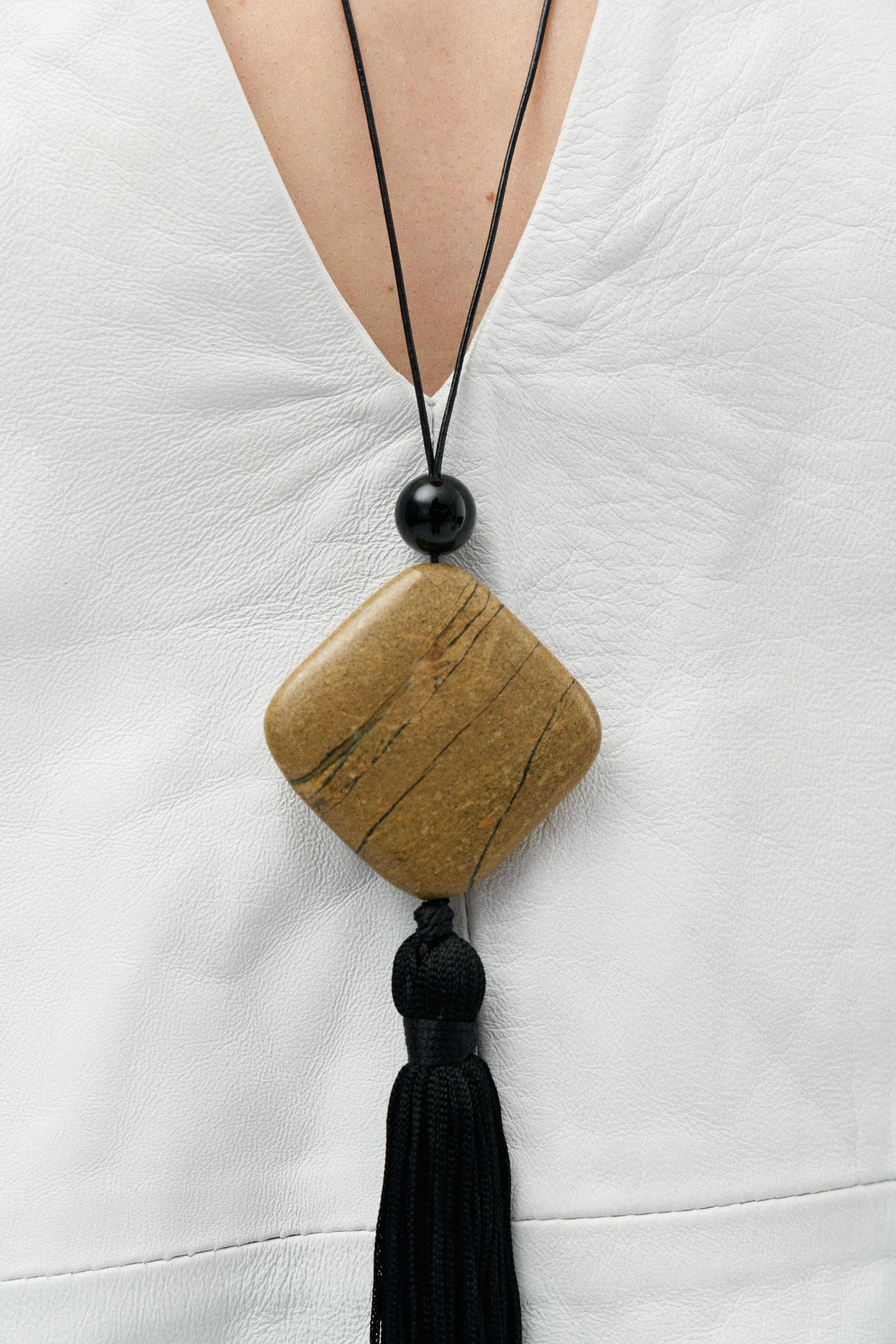 Jasper stone pendant with a black silk tassel against white leather
