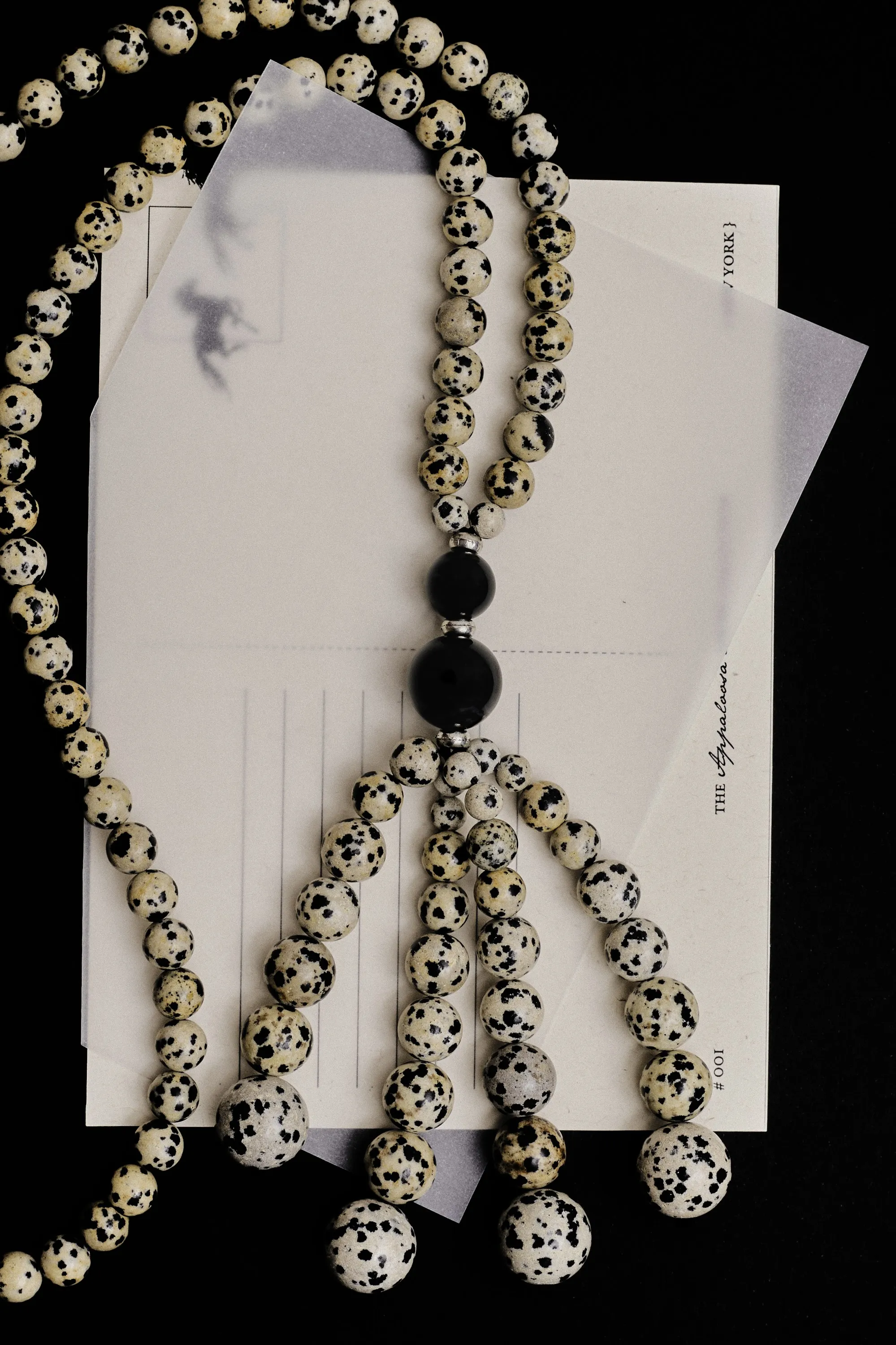 Dalmatian jasper and black onyx bead necklace with tassels over postcards, on black
