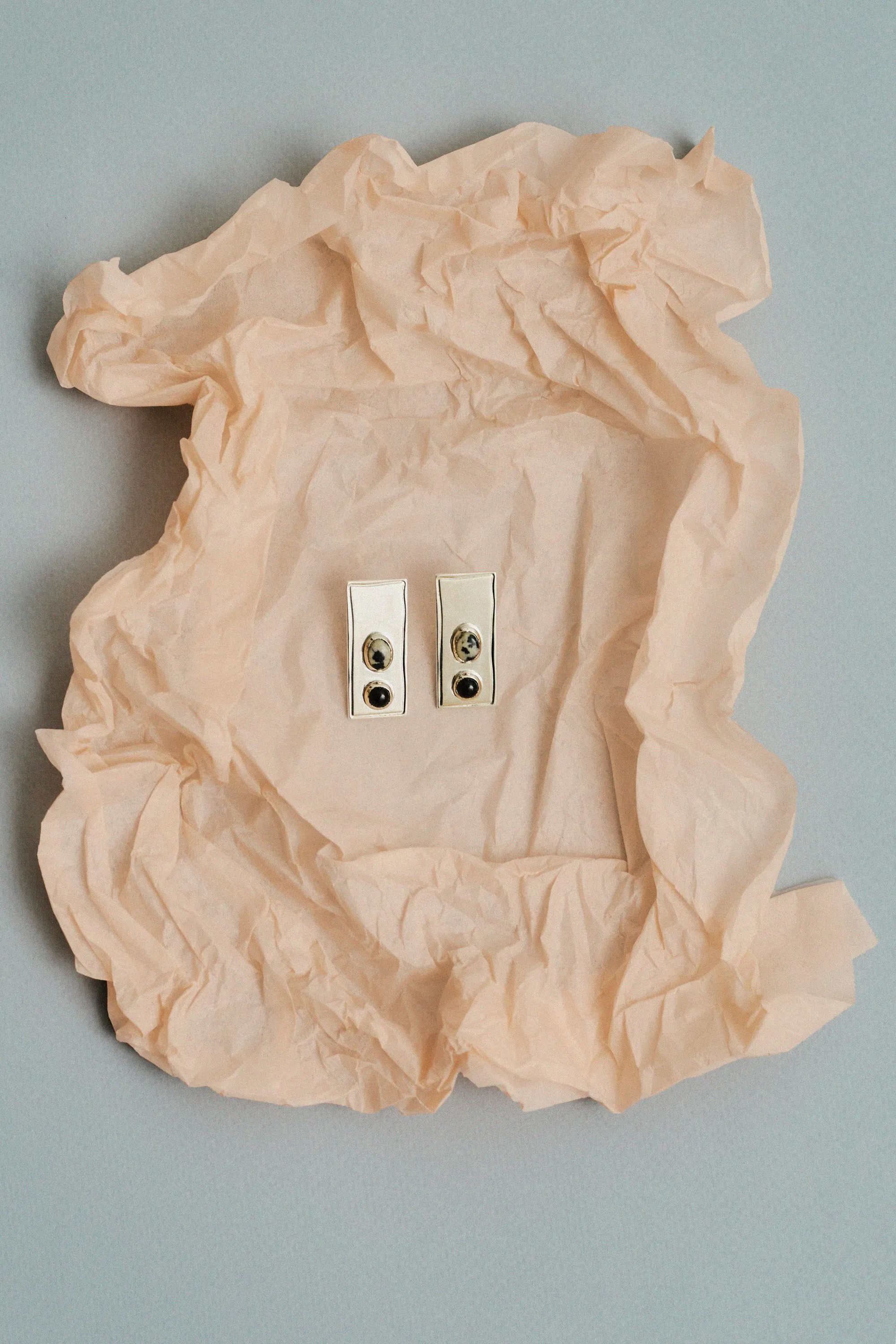 Pair of spotted stone earrings on crumpled peach tissue paper, on pale blue