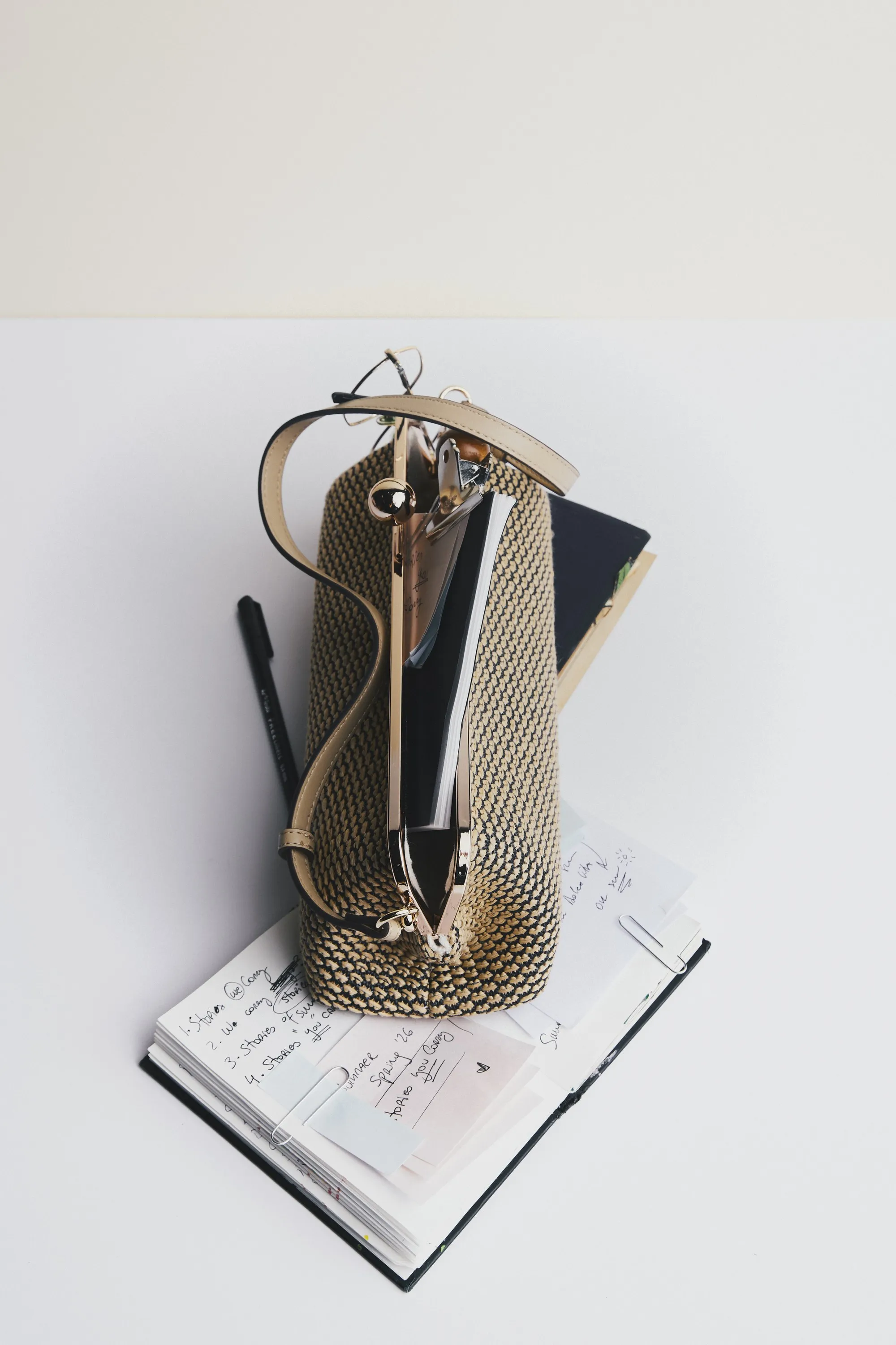 Woven bag holding a notebook and pen, standing on an open journal
