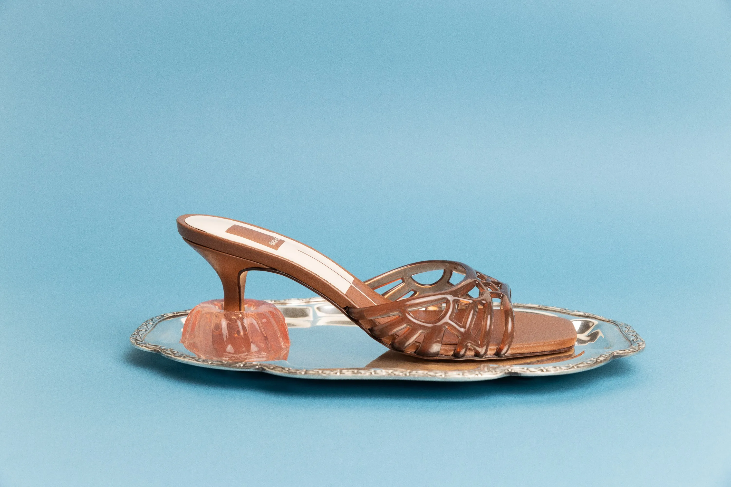 Dolce Vita bronze cutout heel resting on a peach jelly mold on a silver tray, on pale blue