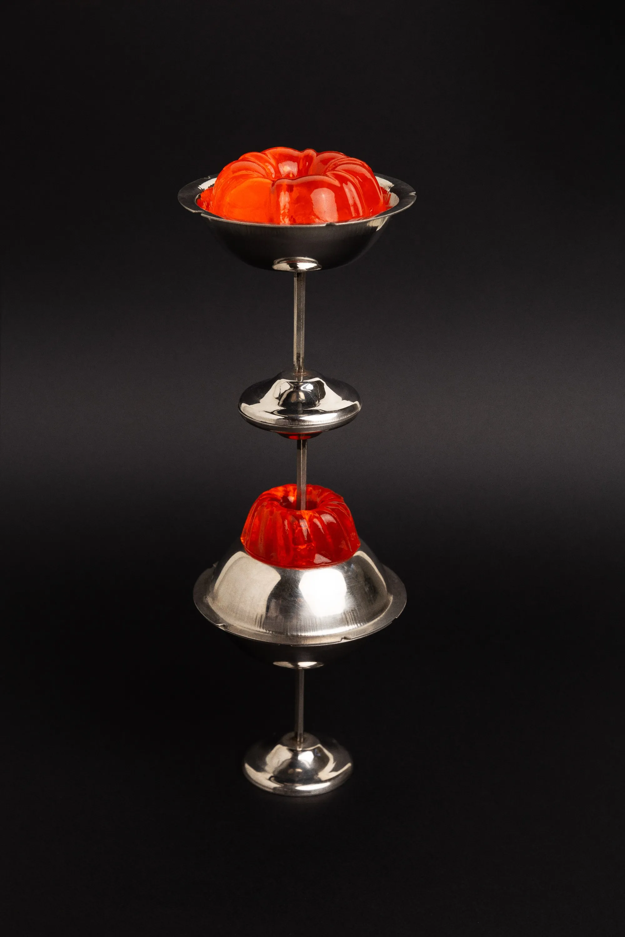 Stacked silver dessert cups holding red jelly molds, on black