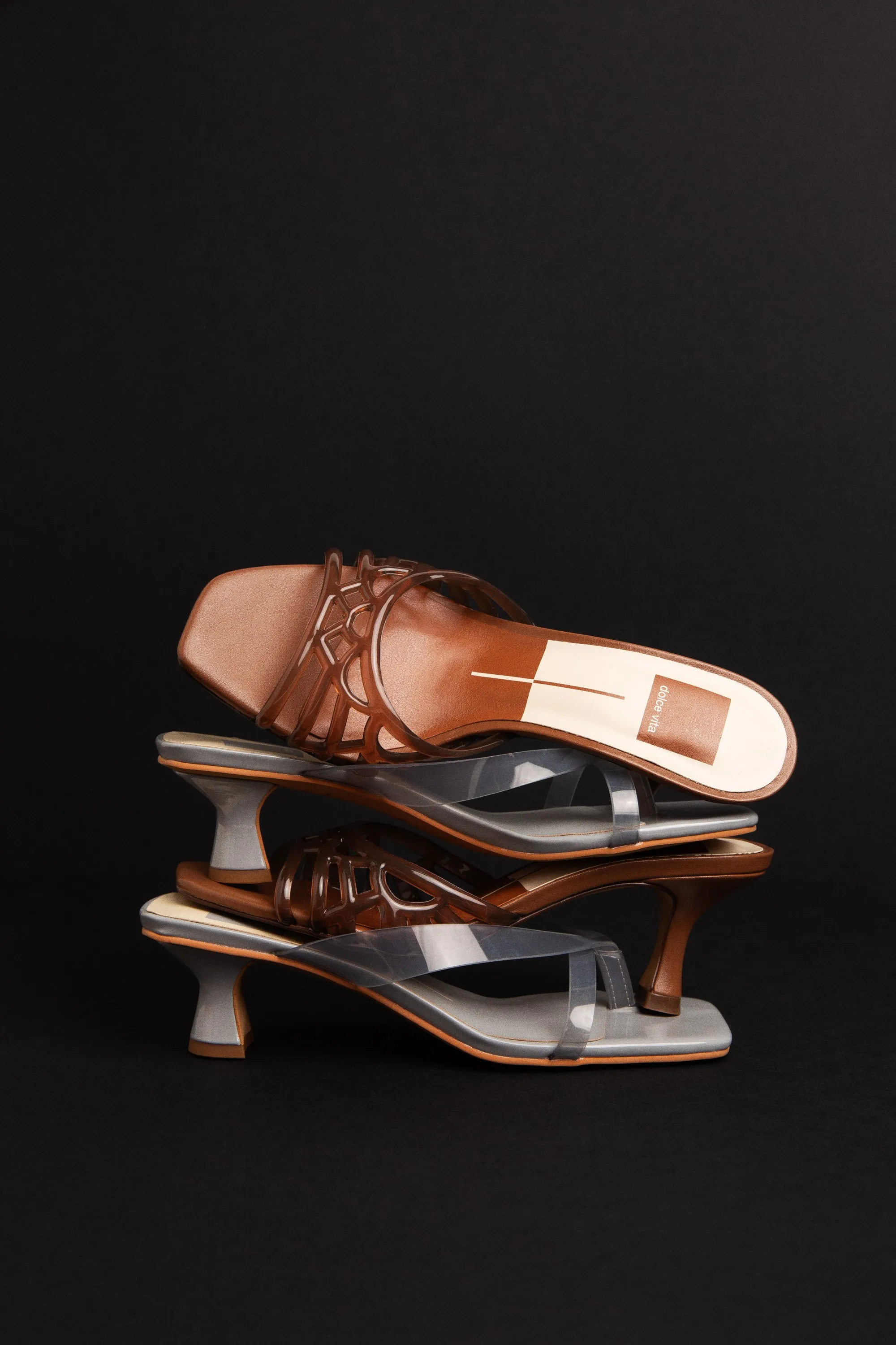 Four Dolce Vita heels stacked in bronze and clear jelly, on black