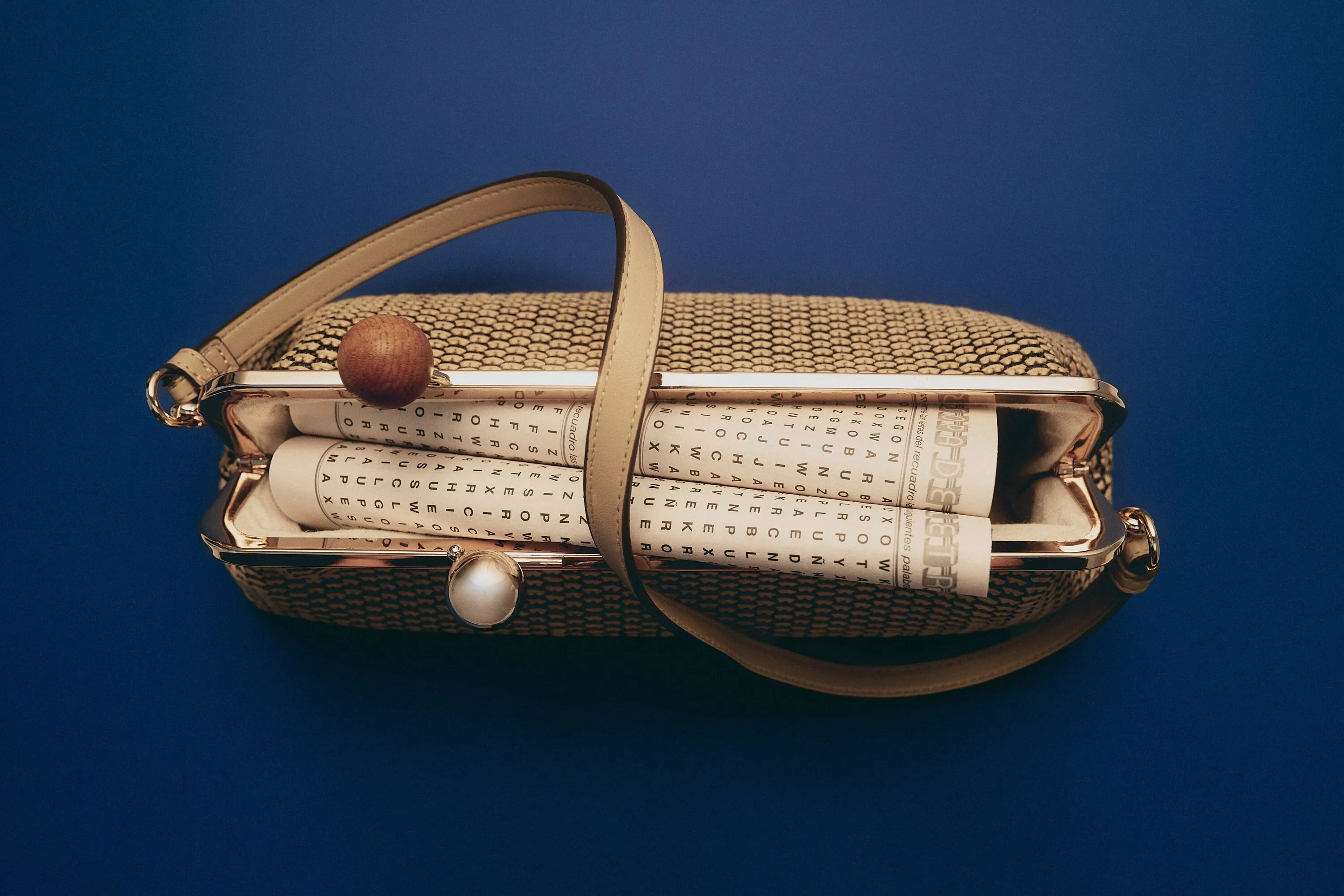 Raffia frame bag holding rolled word-search pages, shot from above on deep blue