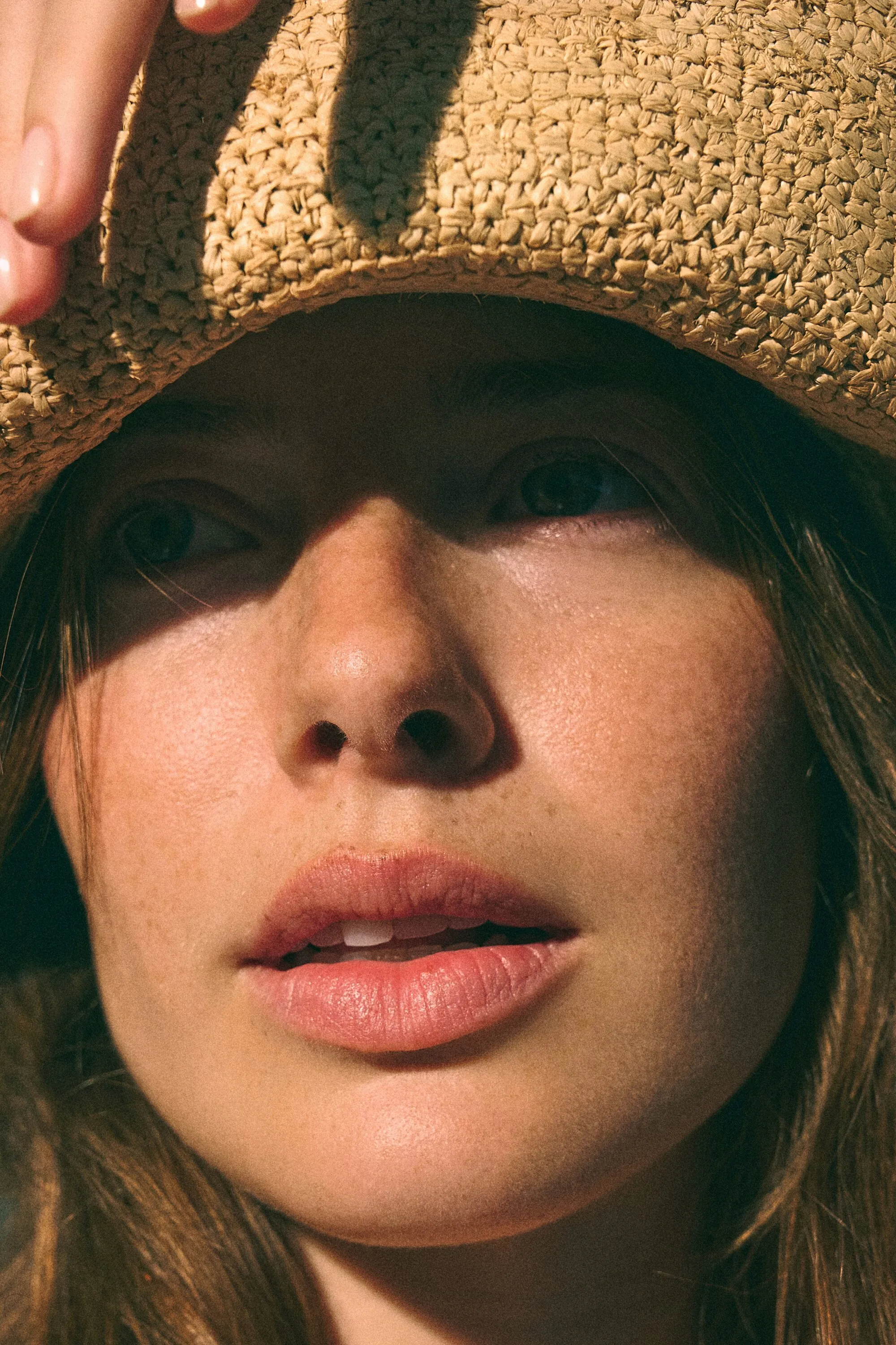 Close-up of a woman's face in the shade of a raffia sun hat