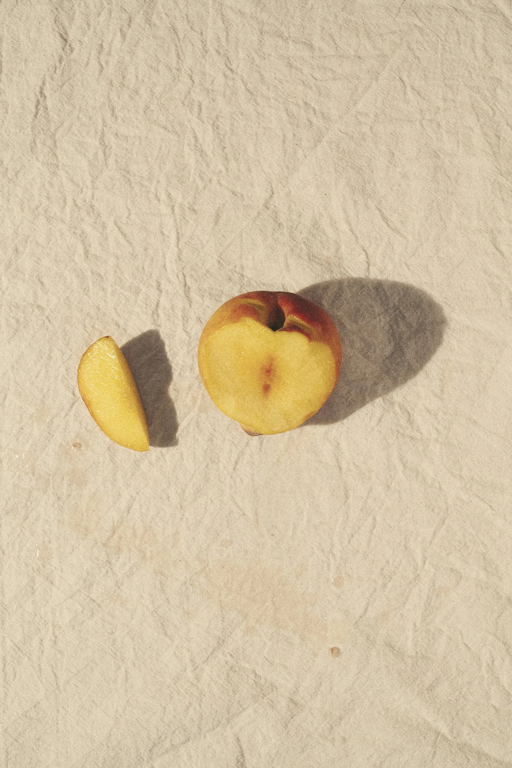 A halved peach casting shadows on crumpled cream paper