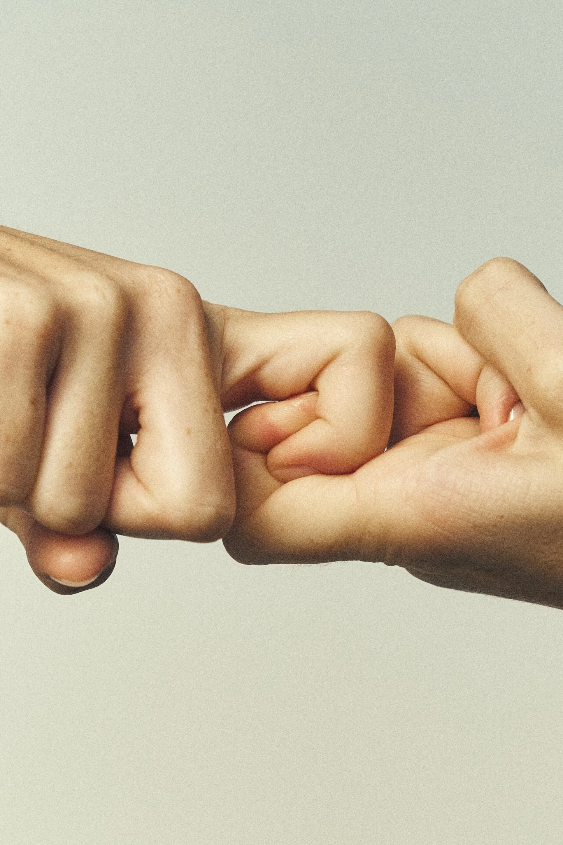 Two hands hooked together by the fingers on a pale grey background