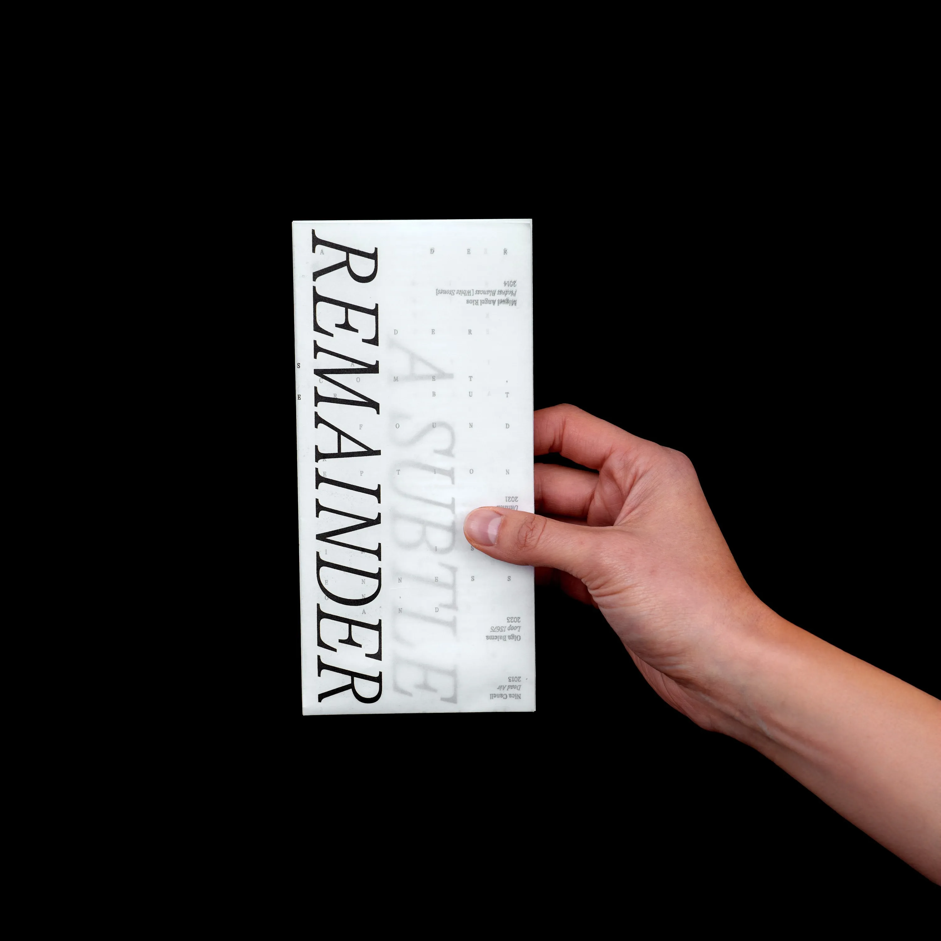 Hand holding the folded A Subtle Remainder booklet on black