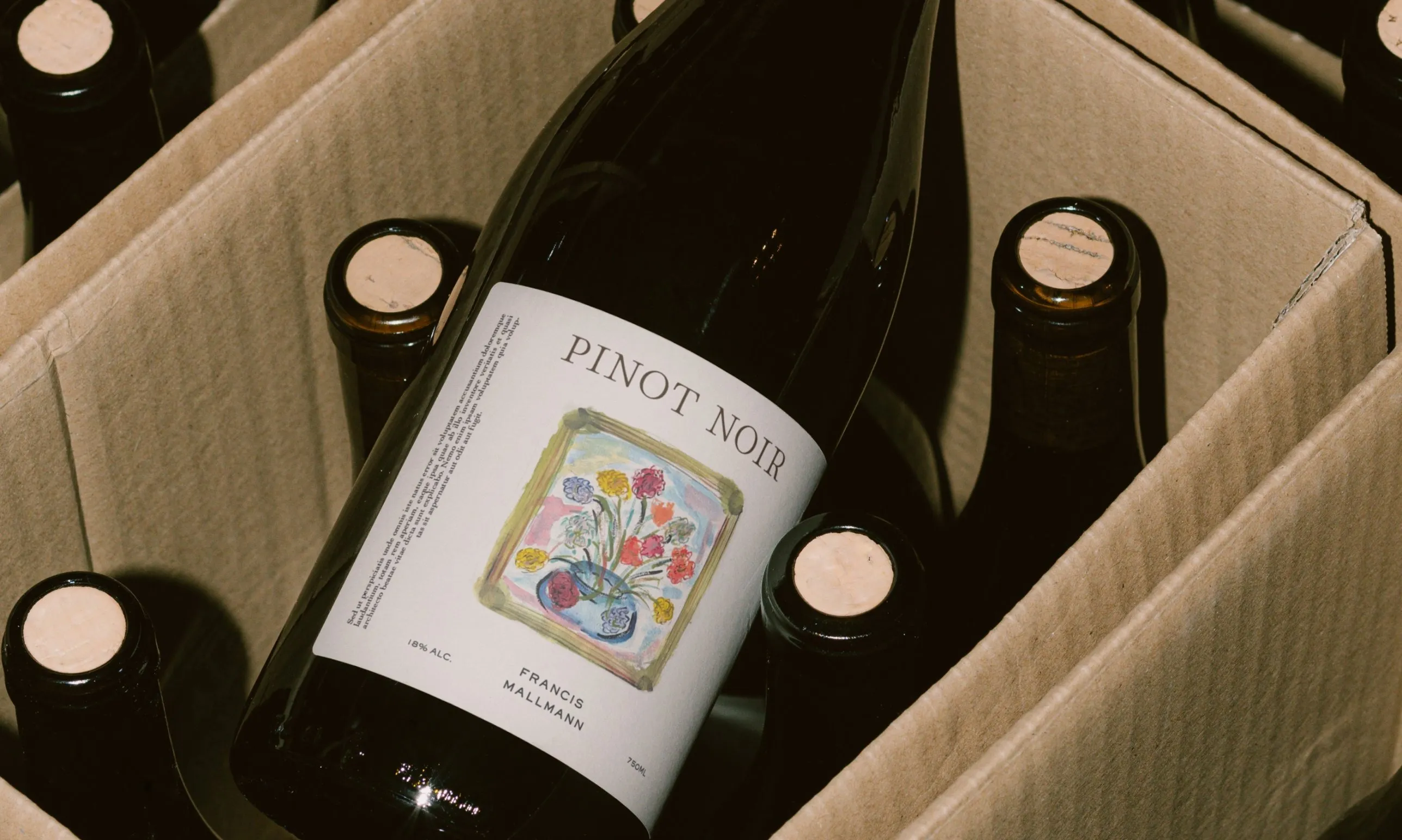 Francis Mallmann Pinot Noir bottle with his painted bouquet on the label, lying in a cardboard case of corked bottles