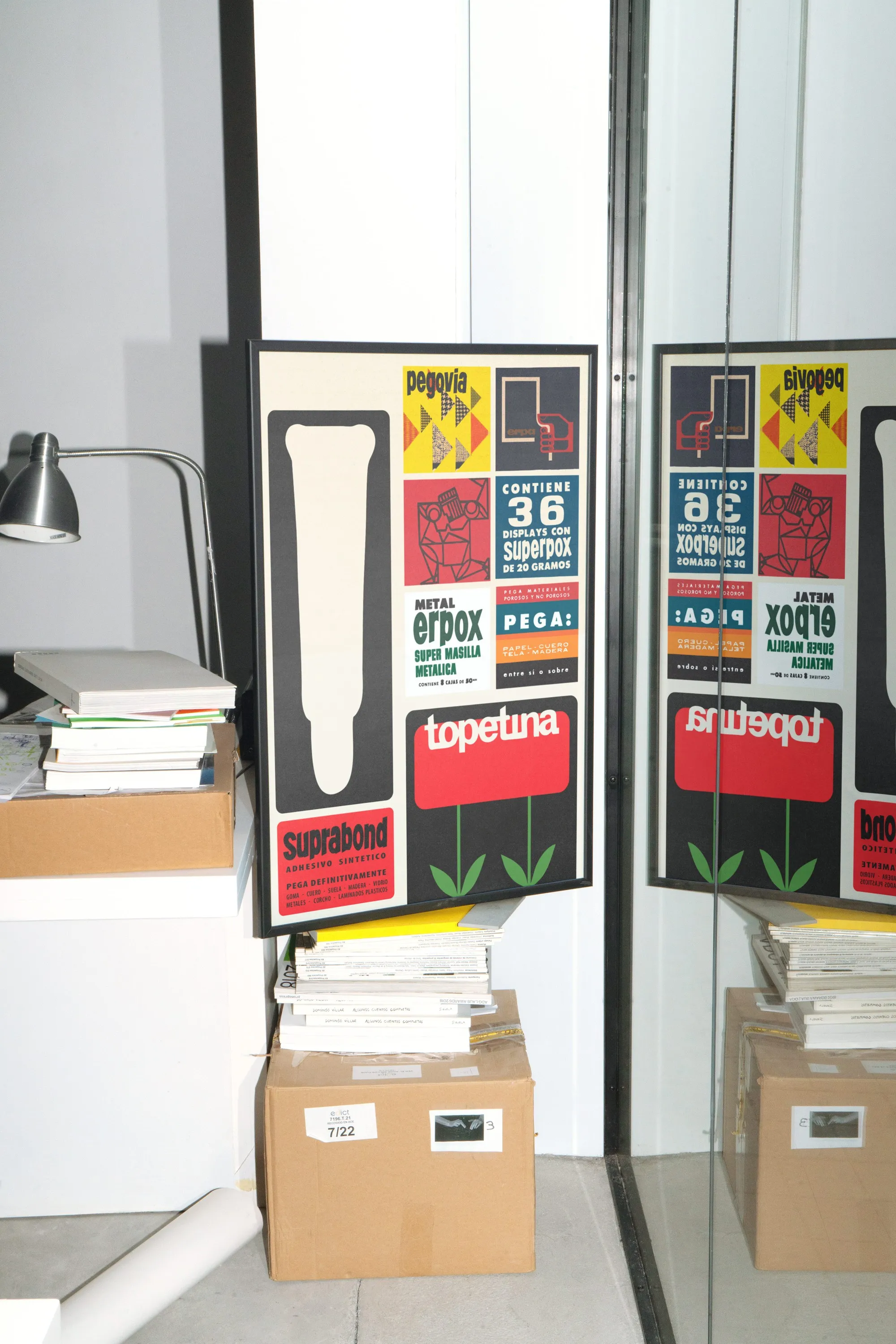 Framed Suprabond product label collage leaning on boxes beside a mirror