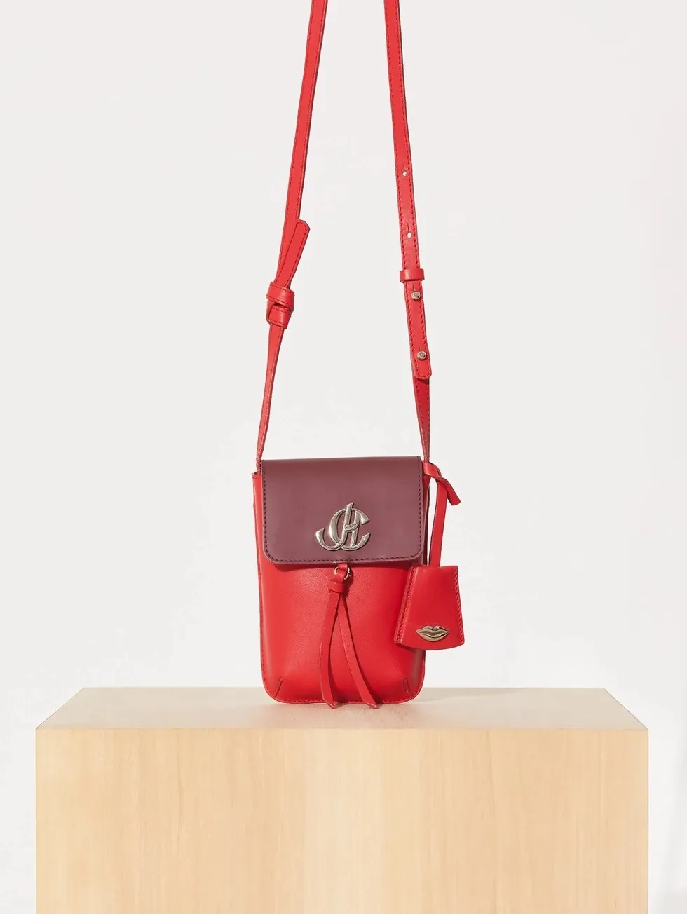Red crossbody bag with silver monogram clasp on a wooden plinth