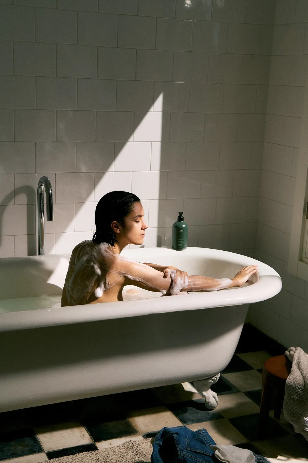 Woman bathing in a clawfoot tub with a Gntl bottle on the rim