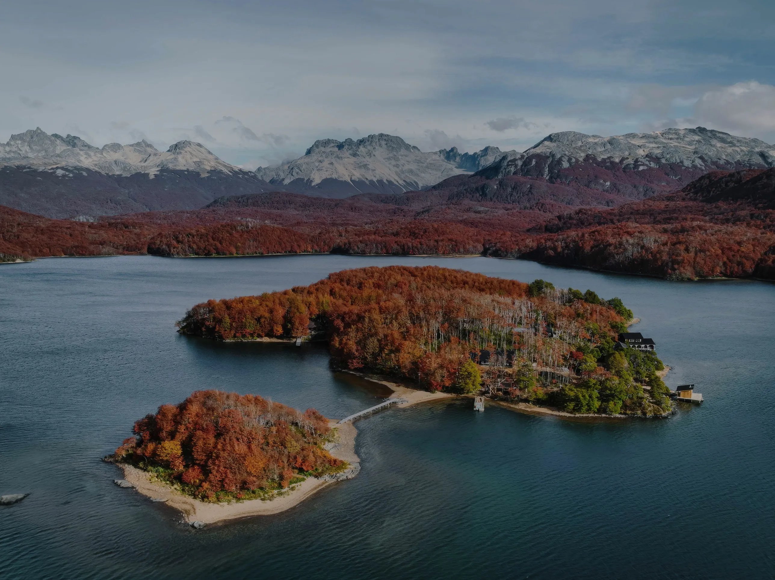 Aerial view of La Isla in autumn, red forest on a lake below snowy peaks