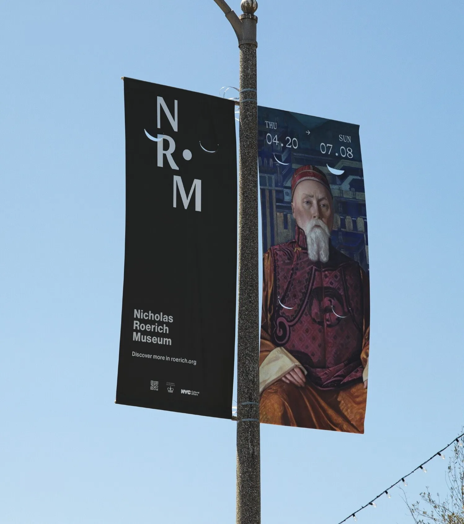 Black NR•M street pole banner next to an exhibition banner with a Roerich portrait