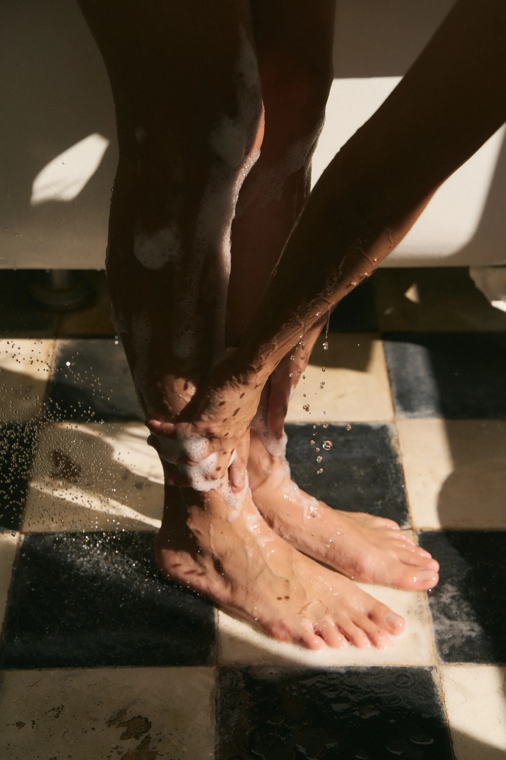 Soapy legs and feet on a black and white checkered tile floor