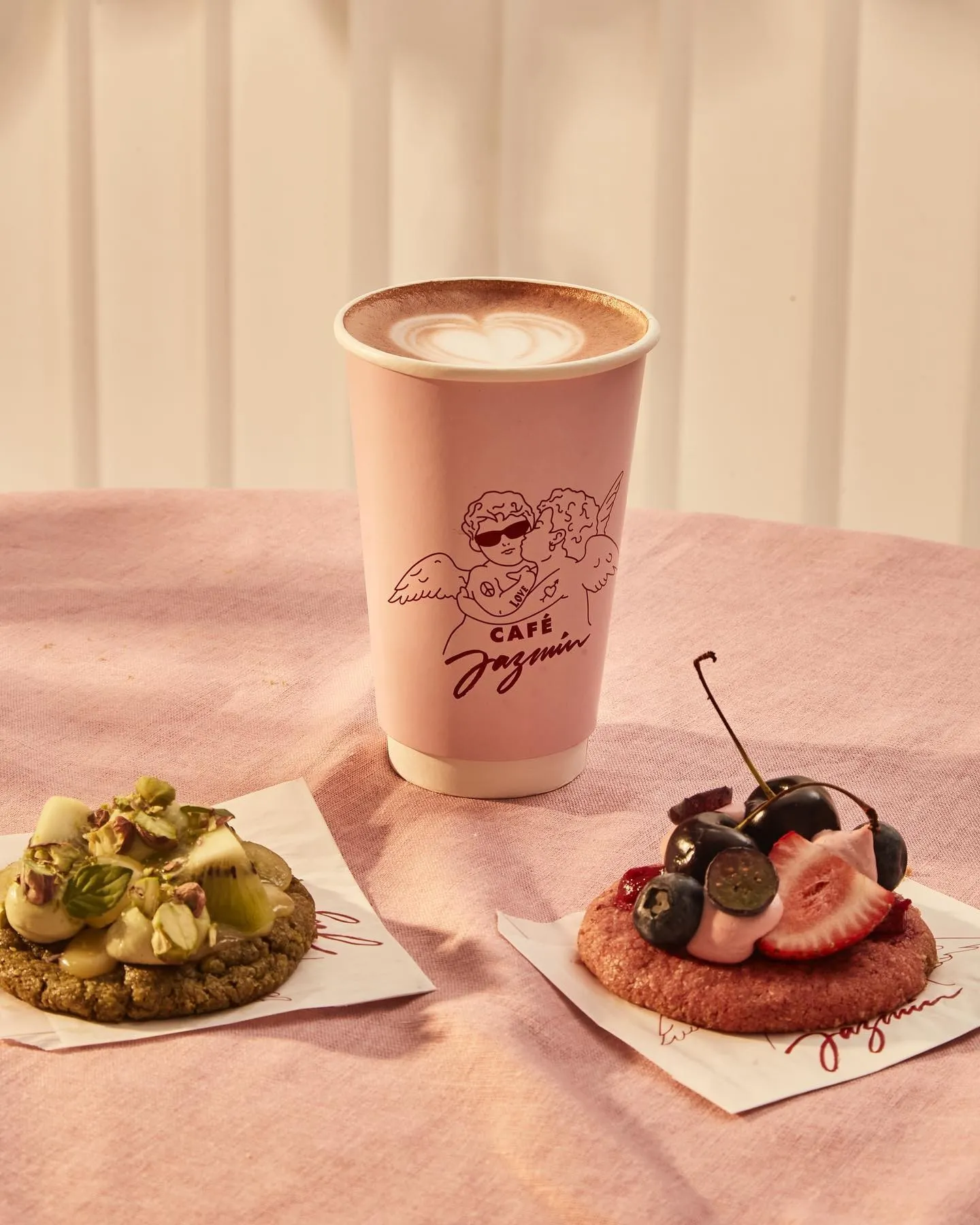 Café Jazmín paper cup with latte art between two topped cookies
